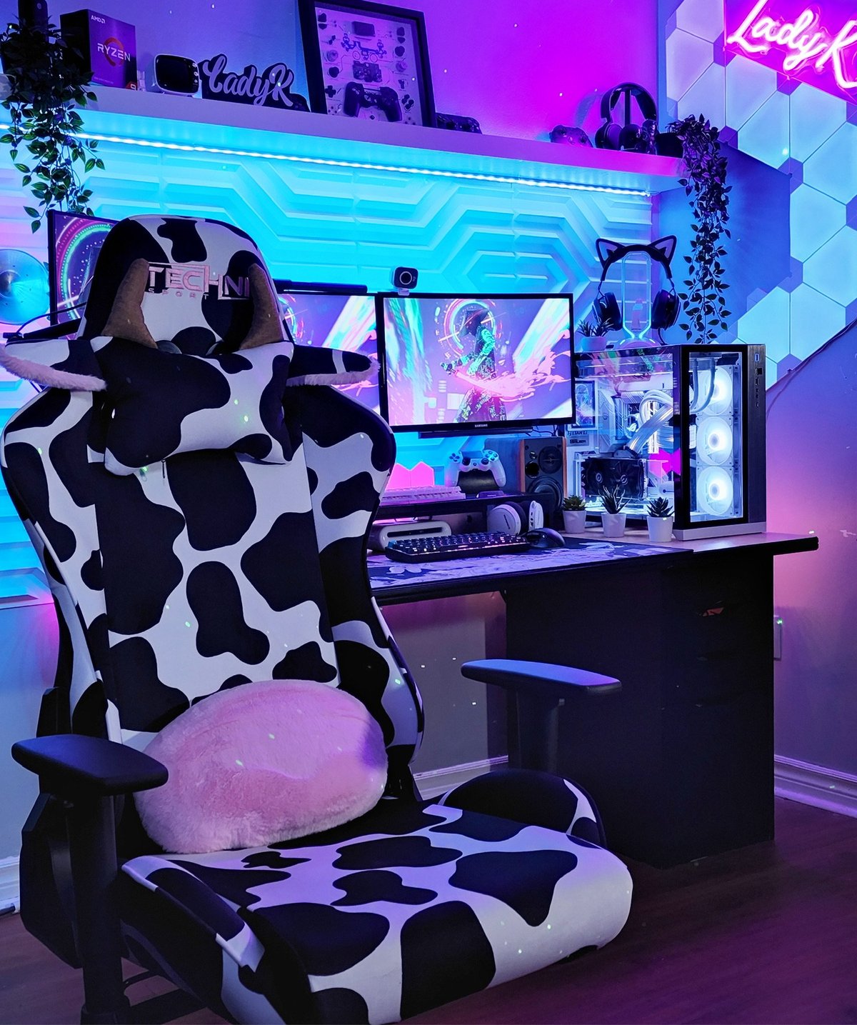 Gaming setup with cow-patterned racing chair, desk with monitor, neon cyan and pink lighting, and decorative elements in modern room